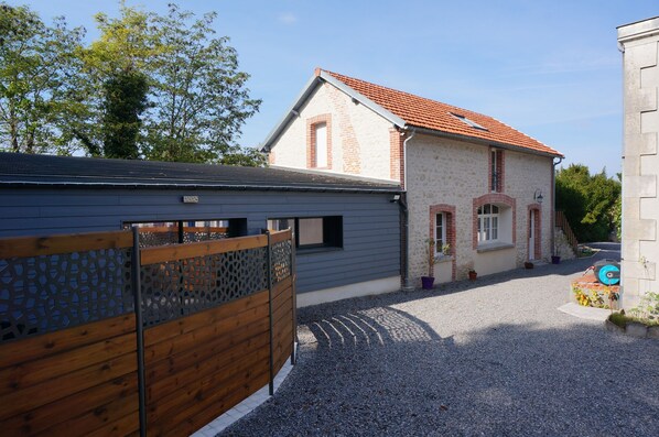 Una casa de dos pisos con techo de tejas rojas, camino de entrada de grava y valla de madera.
