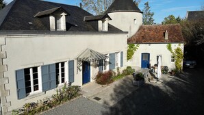 Ein zweistöckiges Gebäude mit weißer Fassade, einer blauen Tür und einem kleinen Garten mit Tisch und Stühlen.