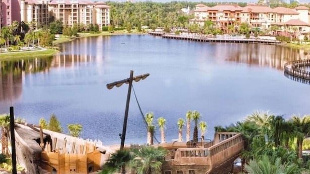 Un resort con una grande piscina, palme e un'attrazione acquatica a tema relitto.