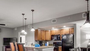 Una cucina moderna con mobili in legno, un frigorifero nero e un forno a microonde. È presente una zona pranzo con tavolo e sedie.