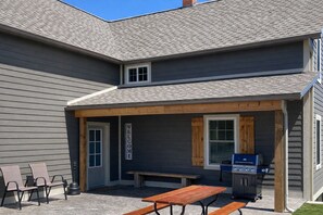 A two-story building with a covered patio area featuring a grill, seating, and a welcome sign.