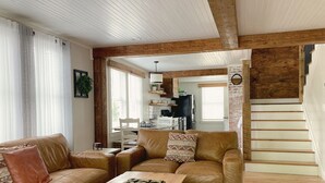 A spacious living room with a brown leather sofa, a wooden coffee table, and a patterned rug. A staircase with wooden steps leads to an upper level.
