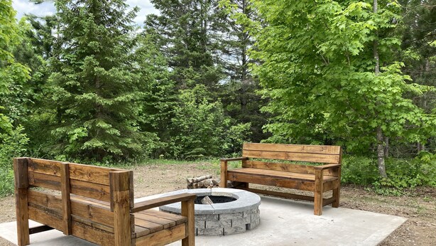 A wooden bench and a stone fire pit in a forested area.