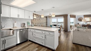 Een moderne keuken met witte kasten, een vaatwasser en een groot eiland. Er is een eethoek met uitzicht op het water.
