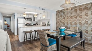 Een moderne keuken met witte kasten, een centraal eiland, barstoelen en een eettafel met blauwe kussens.