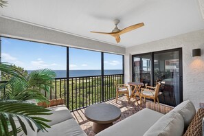 A balcony with a view of the ocean, a ceiling fan, and outdoor furniture.