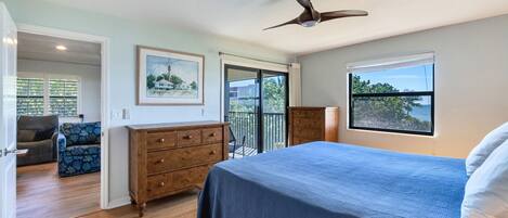 A bedroom with a bed, dresser, ceiling fan, and a balcony with a view.