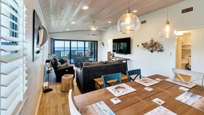 Een moderne woonkamer met een grote televisie, houten vloeren en een eethoek met een houten tafel en stoelen.