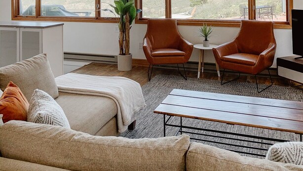 A spacious living room with large windows, a sofa, two leather chairs, a coffee table, and a potted plant. - Reservoir Retreat with Hot Tub and Mtn. Views! (Fort Collins)