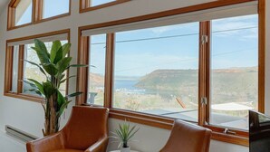 A room with large windows, a plant, two leather chairs, a small table, and a TV. - Reservoir Retreat with Hot Tub and Mtn. Views! (Fort Collins)