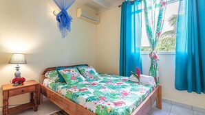 A bedroom with a bed, a nightstand, a lamp, a mosquito net, and curtains. - Cottage La Perle  ( pool, BBQ, view on moutains, sea, rivers, forests) (Basse-Terre)