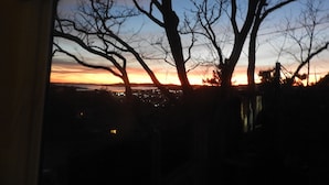 Blick durch ein Fenster auf kahlstehende Bäume vor einem Sonnenuntergangshimmel.