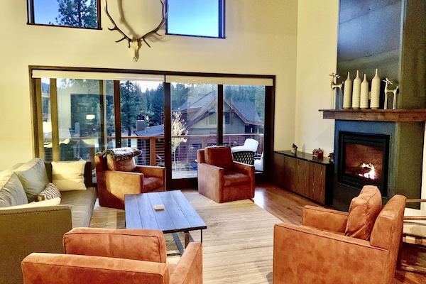 Large open great room with balcony, and 4 plush swivel chairs around fireplace.