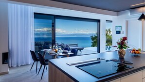 A modern kitchen with a large island, a dining area with a view of the sea, and a large sliding glass door. - Sky Pool Villa Medveja: heated pool, spa, sea view (Medveja)