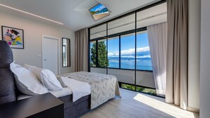 A modern bedroom with a large window offering a scenic view of the sea and a cityscape. - Sky Pool Villa Medveja: heated pool, spa, sea view (Medveja)