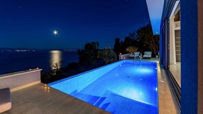 Ein moderner Infinity-Pool mit Blick auf das Meer in der Nacht.