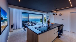 A modern kitchen with a large island, a dining area with a view of the sea, and a minimalist decor. - Sky Pool Villa Medveja: heated pool, spa, sea view (Medveja)