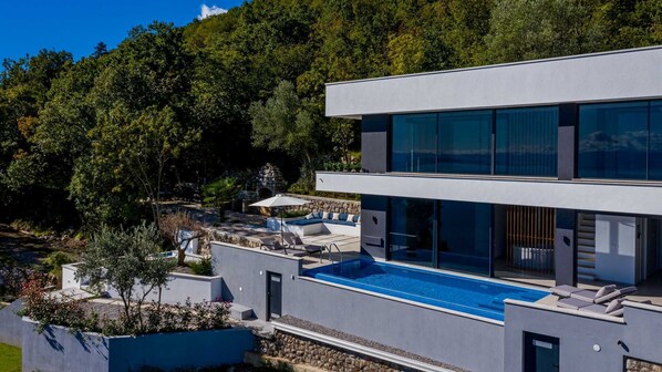 Ein modernes, zweistöckiges Gebäude mit Pool auf dem Dach, umgeben von üppiger Vegetation.
