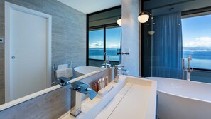 Ein modernes Badezimmer mit einer großzügigen Badewanne, zwei Waschbecken und Meerblick.