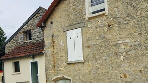 Un edificio de piedra con camino de grava, una puerta de madera y una ventana con contraventanas.