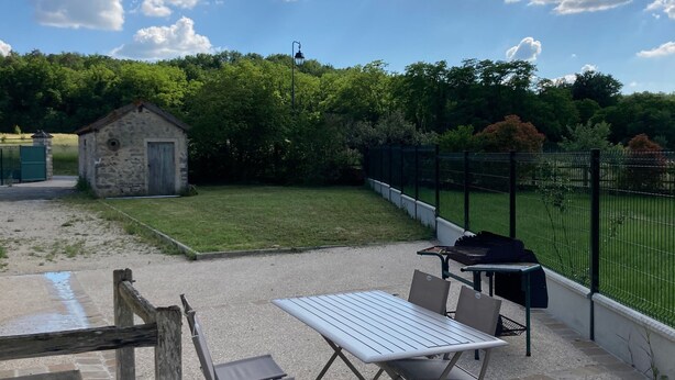 Un patio al aire libre con una mesa y sillas, un edificio de piedra y un campo deportivo cercado.