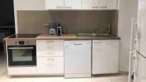 Una cocina moderna con armarios blancos, horno integrado, lavavajillas y encimera con cafetera y otros electrodomésticos.