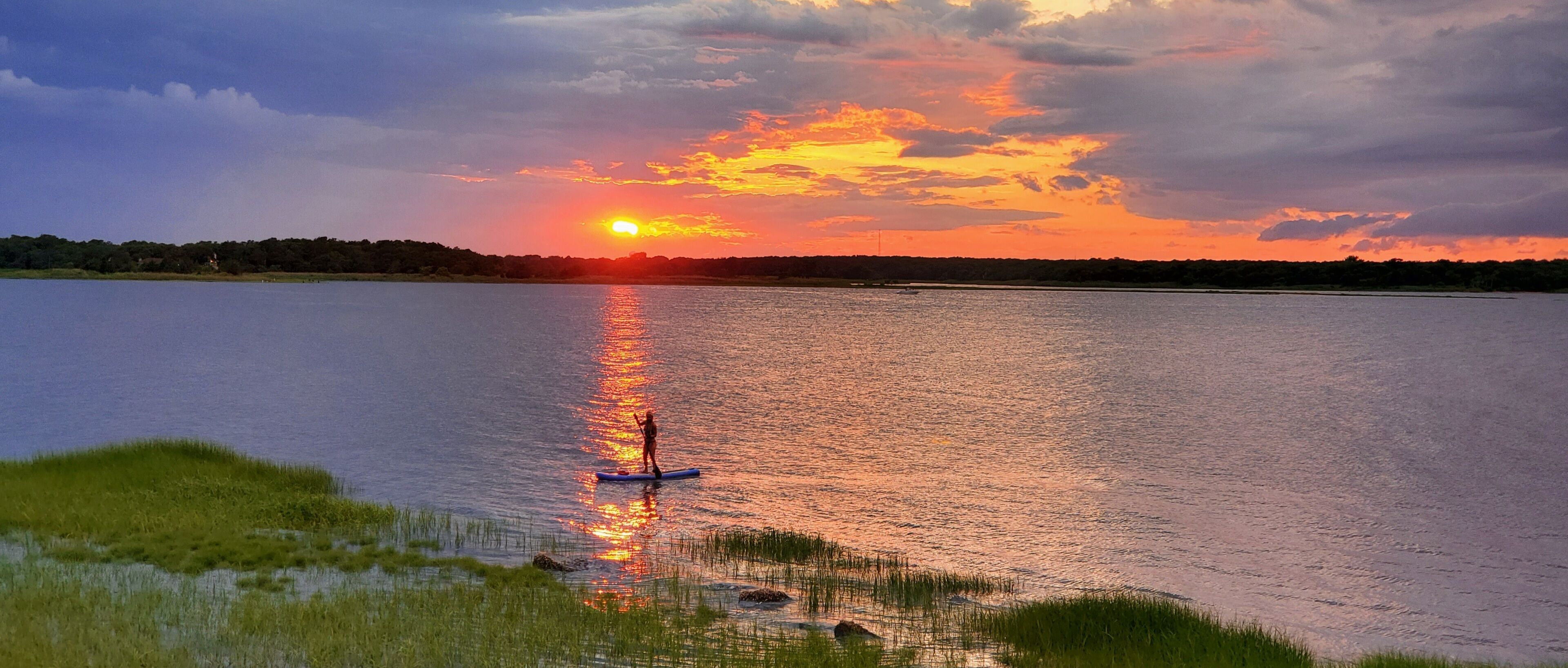 A sunset over a calm lake with a paddleboarder.