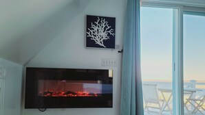 A living room with a fireplace, a framed artwork, and a view of a deck through a sliding glass door.