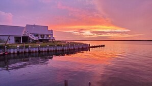 A waterfront property with a large house featuring a balcony and a dock extending into the water.