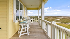 A wooden deck with white railings, a row of Adirondack chairs, and a view of a coastal landscape.