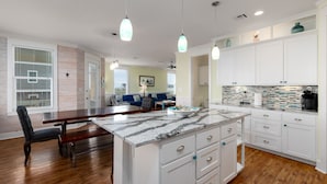 A spacious kitchen with white cabinets, a granite countertop, and pendant lighting.