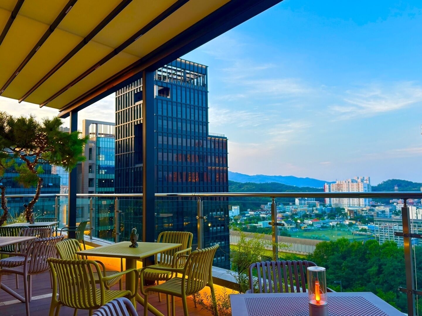 Un espacio al aire libre con mesas y sillas, con vistas a un paisaje urbano de edificios modernos y colinas distantes.
