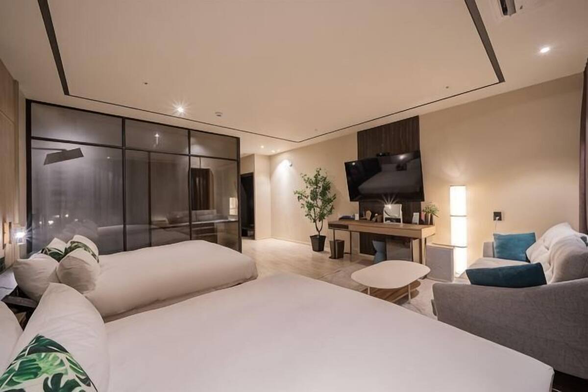 A modern hotel room with a large bed, a sofa, a TV, and a desk.
