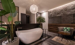 A modern bathroom with a freestanding bathtub, a large potted plant, and a unique textured wall. - Daegu Eastern Hotel Lions Park (Daegu)