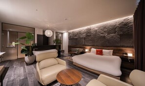 A modern hotel room with a large bed, a seating area with a round table, and a stone accent wall.