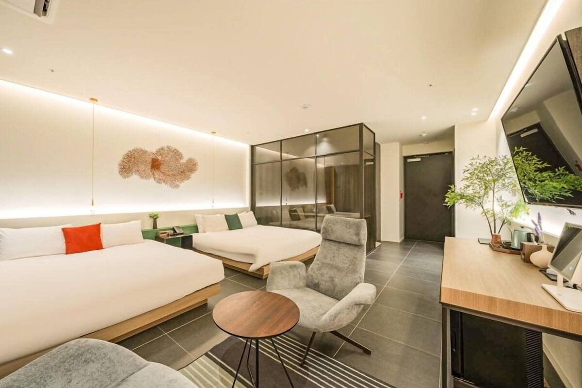 A modern hotel room with two beds, a seating area, a desk, and a large mirror.
