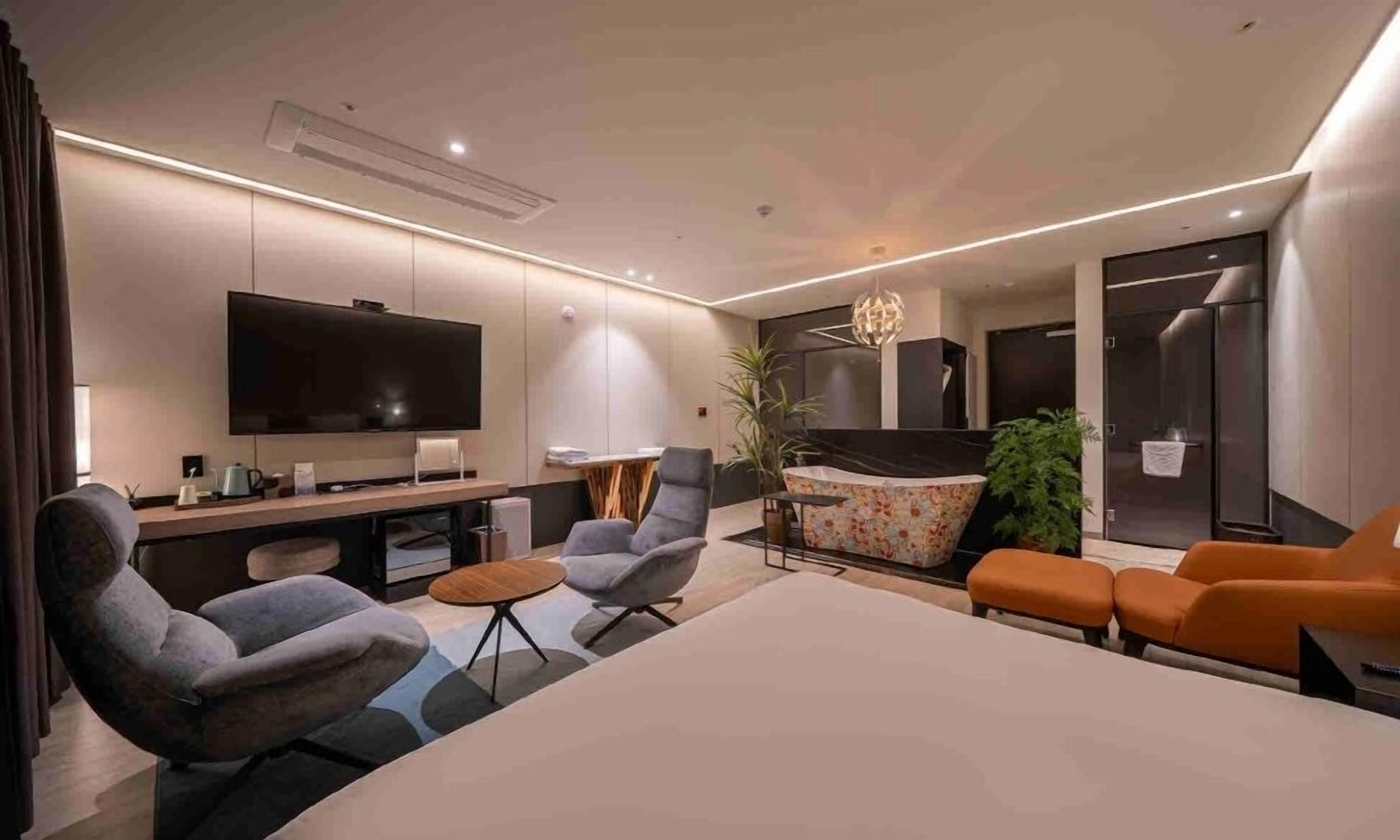 A modern living room with a flat-screen TV, comfortable seating, a dining area, and a kitchen.