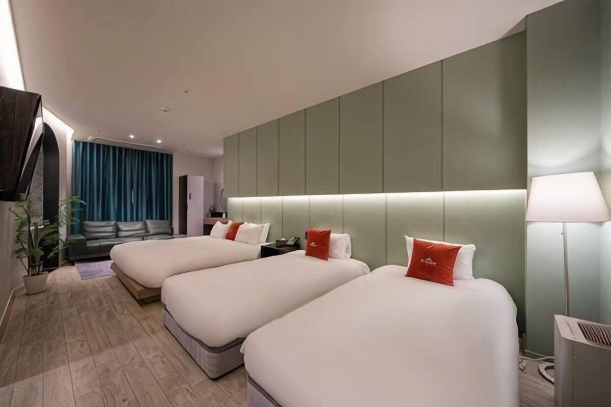 A hotel room with two beds, a sofa, a desk, and a lamp.