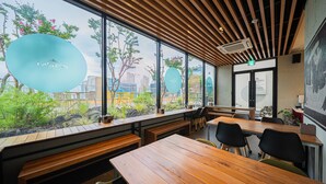 A modern restaurant with wooden tables and benches, large windows with views of greenery and buildings, and a ceiling with wooden slats. - Daegu Eastern Hotel Lions Park (Daegu)