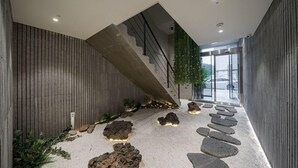 A modern interior with a concrete staircase, a stone pathway, and a view of the outside through a glass door. - Daegu Eastern Hotel Lions Park (Daegu)