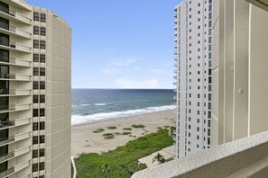Ein Hochhaus mit mehreren Balkonen mit Blick auf einen Strand, der von Wellen und viel Grün geprägt ist.