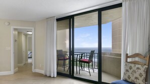 Un balcon avec vue sur l’océan, un coin repas avec des chaises et une chaise en bois avec un coussin.