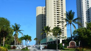 Un grand hôtel moderne, doté de nombreux étages et de balcons, entouré de palmiers et d’un parking clôturé.