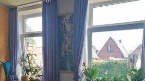 Et hyggeligt værelse med en seng, en stol, en reol og et vindue med gardiner.