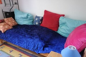 Un lit recouvert d’un tissu de velours bleu, plusieurs oreillers de différentes couleurs et une tête de lit en bois.