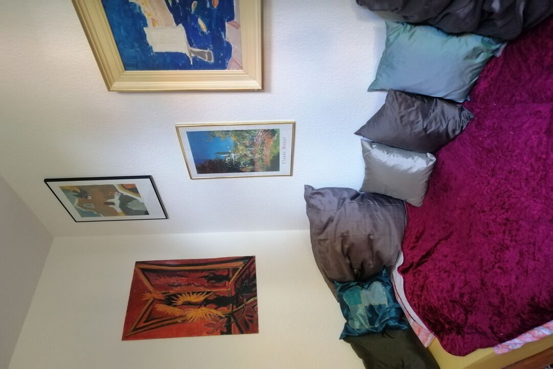 A room with a bed, pillows, and three framed artworks on the wall.
