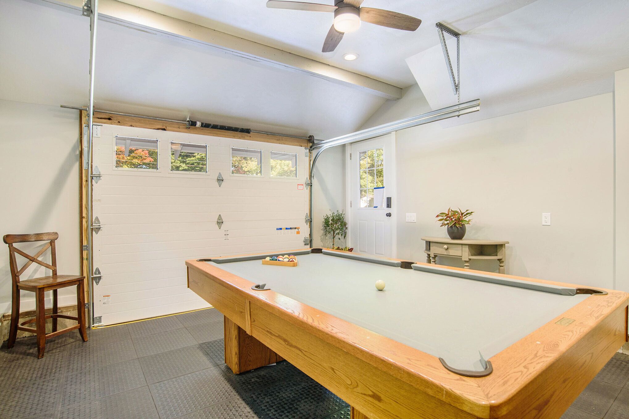 Ein Billardtisch mit Holzrahmen, ein Deckenventilator und eine Tür mit Fenstern.