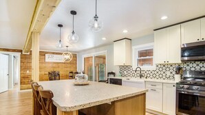 Una cocina con una isla grande, sillas de madera, horno de acero inoxidable y luces colgantes.