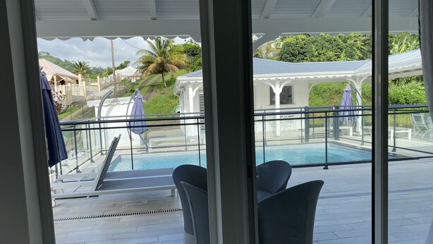 A poolside area with a glass balustrade, two lounge chairs, and a view of a swimming pool. - Villa Rubis equipped for people with reduced mobility  (Gourbeyre)