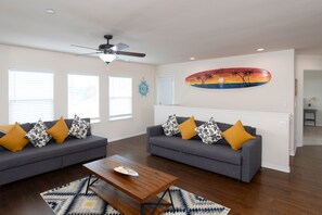 A living room with two grey sofas, yellow and patterned cushions, a wooden coffee table, and a ceiling fan.